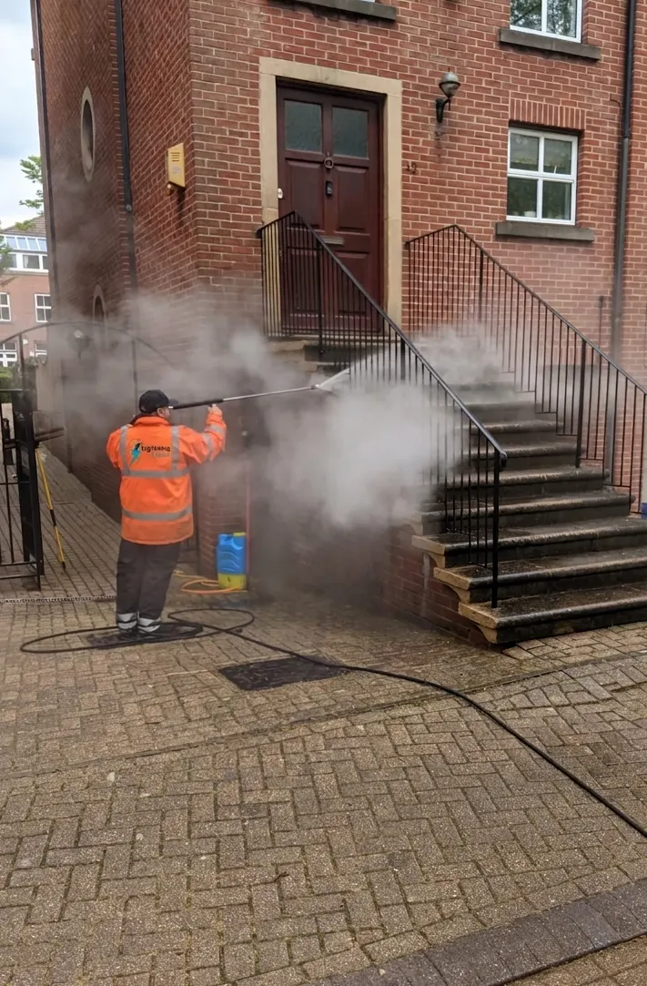 Lightning Clean technician in hi-vis steam cleaning the steps outside a brick building